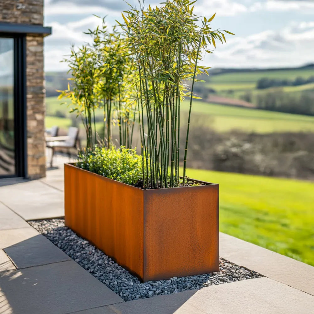 Corten steel trough planter with green plants on a patio area with a scenic background