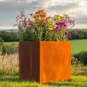 Orange metal planter with colorful flowers in a natural setting