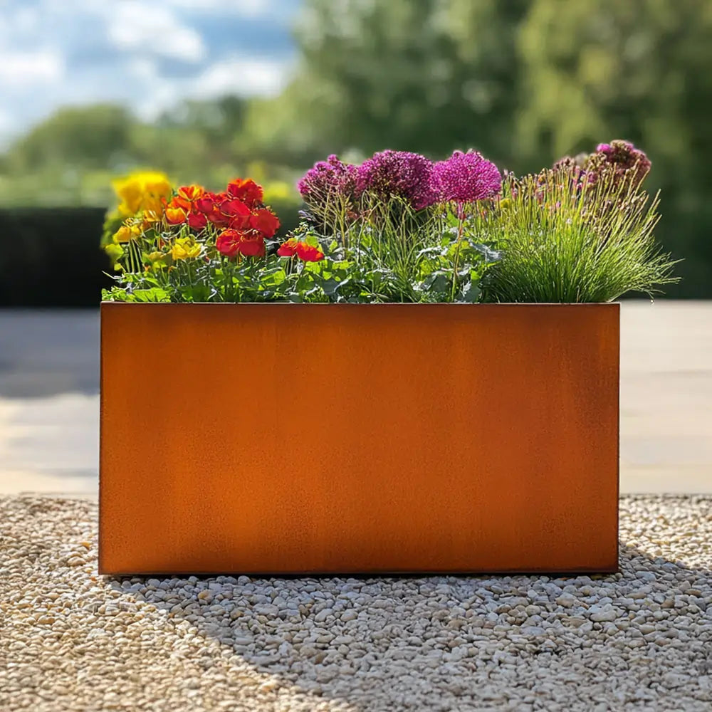 Orange metal planter with colorful flowers on a pebble surface