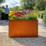 Orange metal planter with colorful flowers in a garden setting