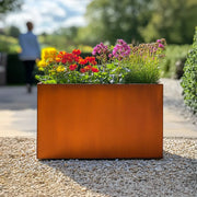 Orange metal planter with colorful flowers in a garden setting