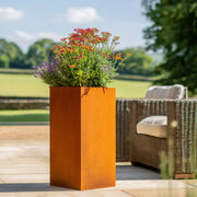 Tall rust-colored Corten planter with flowers on a patio