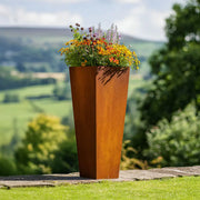 Rust-colored metal planter with flowers against a scenic background