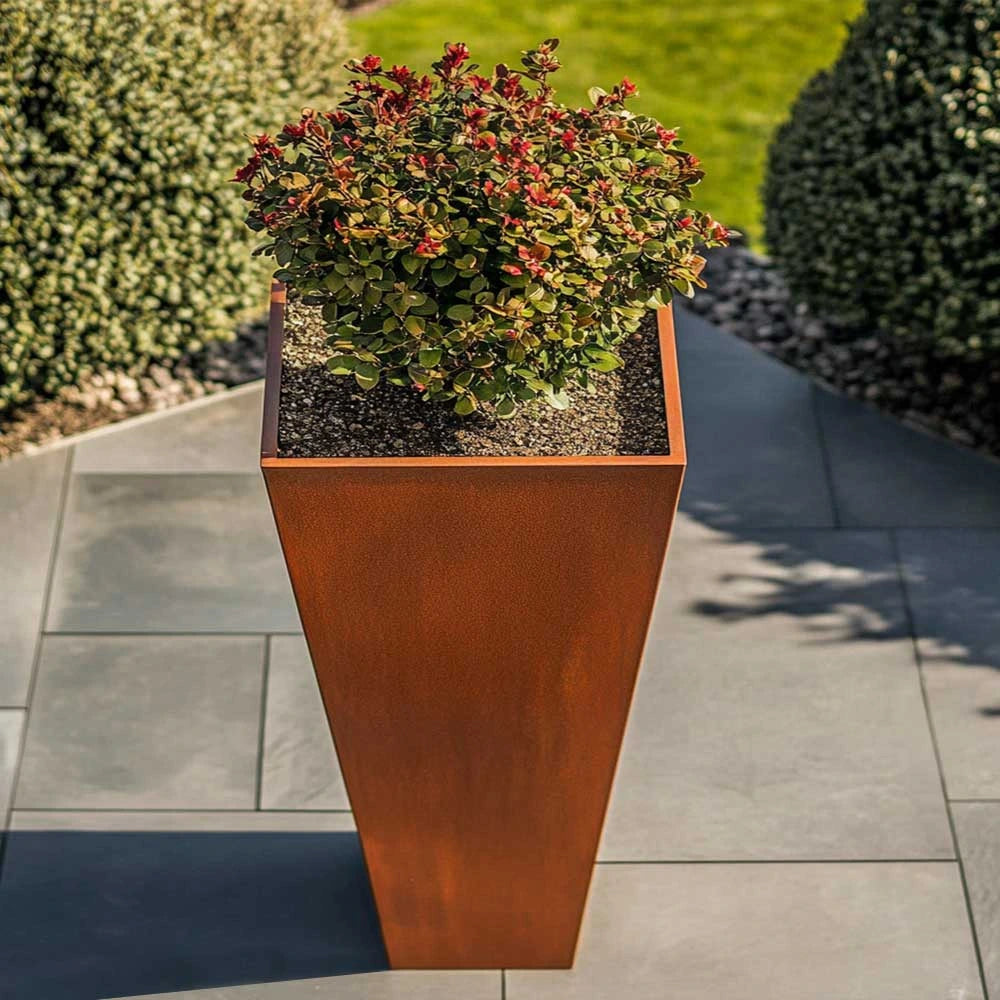 Tall rust-colored planter with a bush on a stone patio