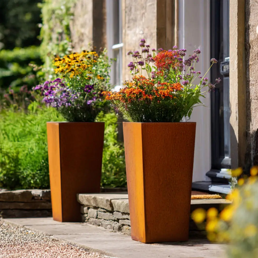 Two rust-colored corten planters with flowers on a wooden deck.