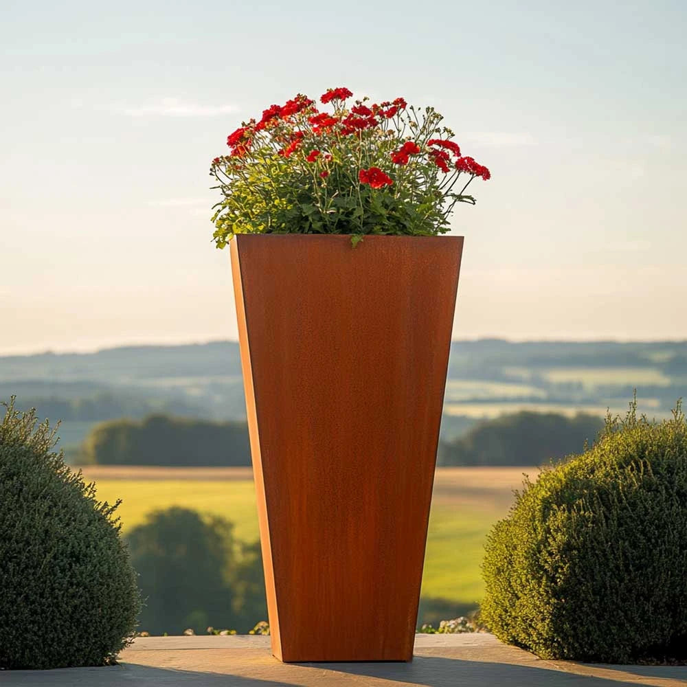 Tall metal planter with red flowers against a scenic background