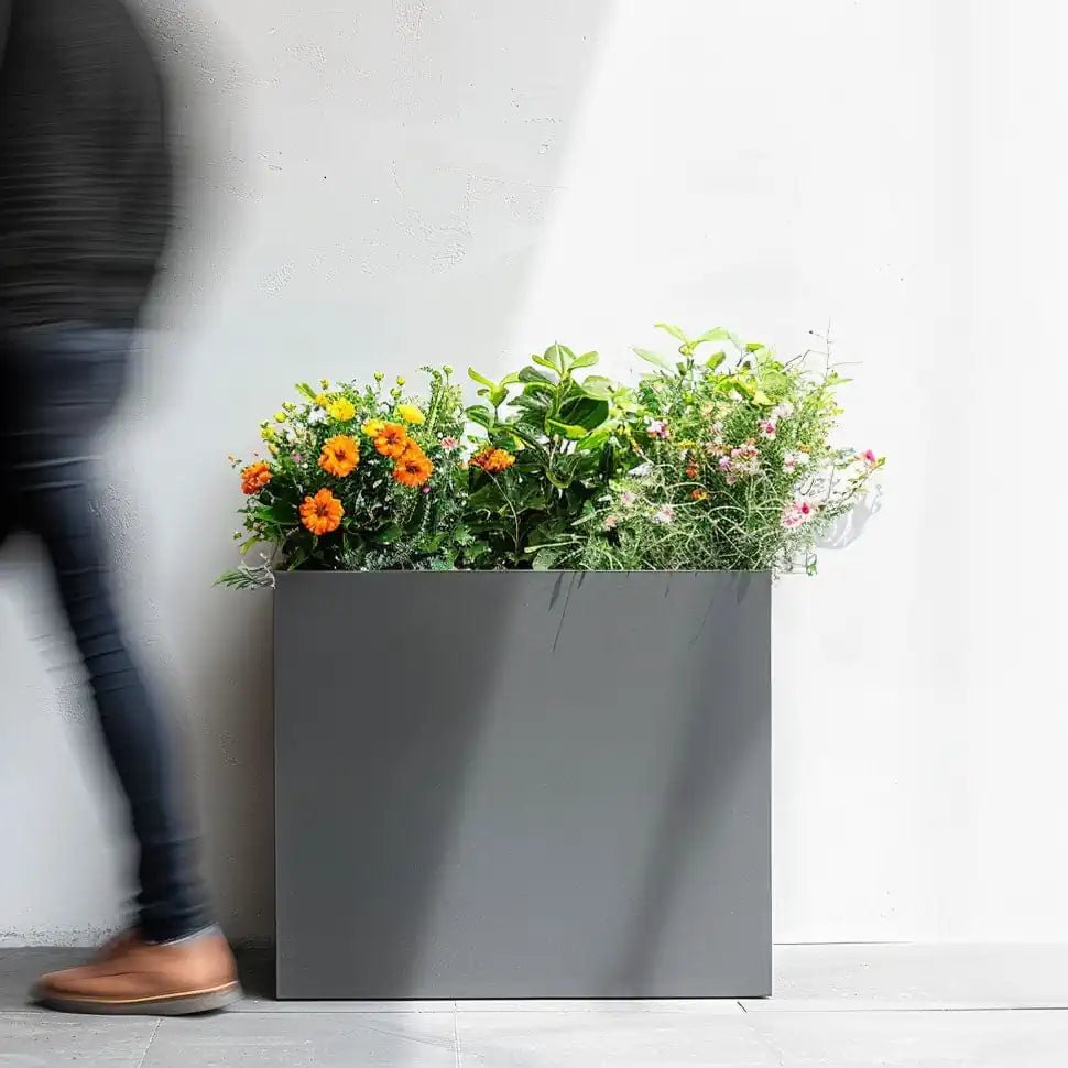 A person walking past a grey long tall plant pot.